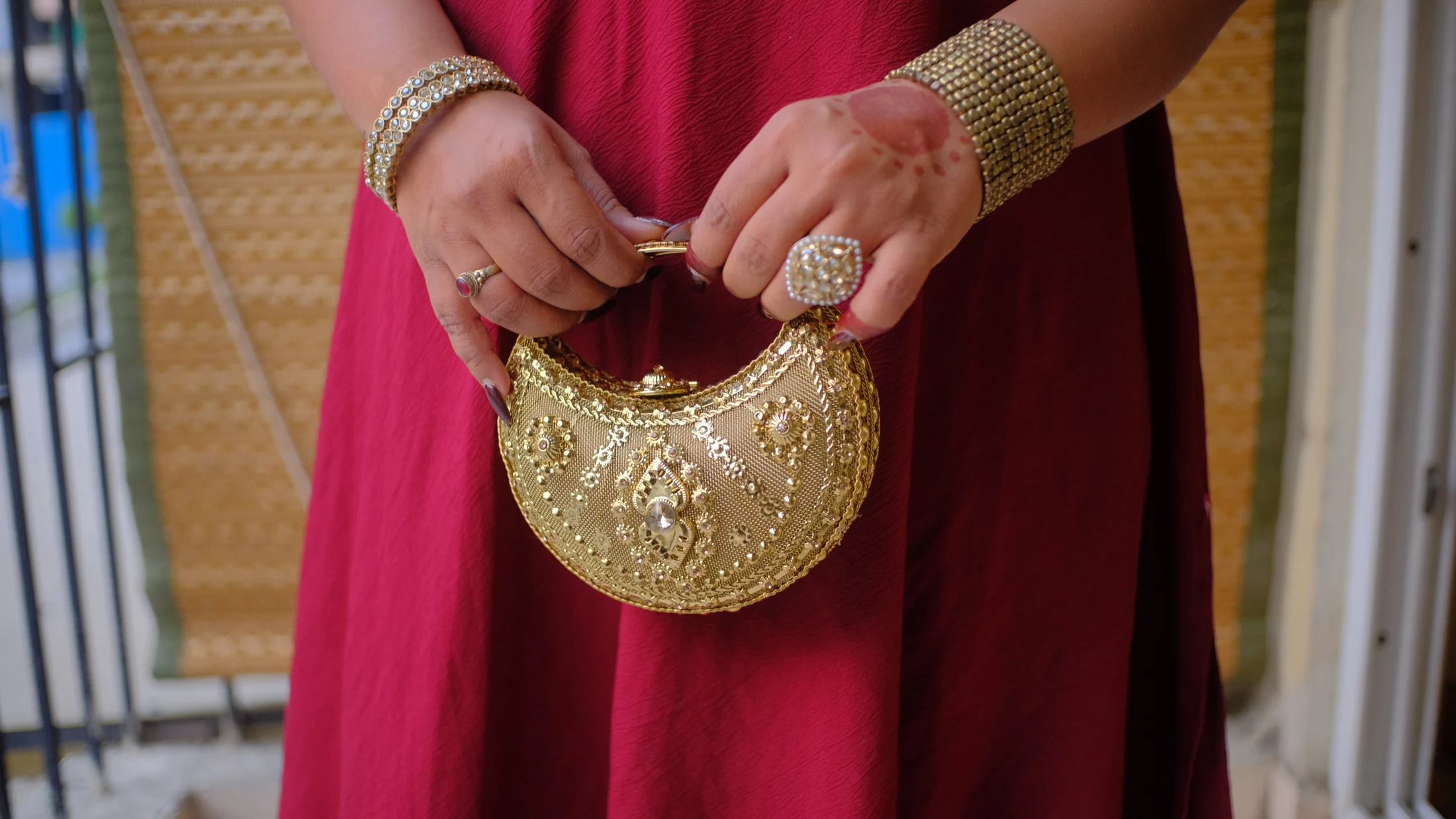 Adaah's gold crescent bag carried against crimson fabric, with detailed gold jewellery